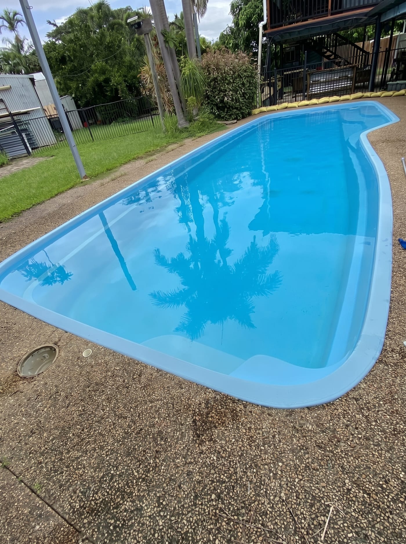 Crystal-clear fibreglass pool in a Townsville backyard after a Basic Pool Service visit, with palm tree reflections on the water